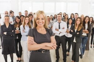 Smiling business woman standing with her arms crossed and looking at the camera. Large group of her colleagues are in the background. [url=http://www.istockphoto.com/search/lightbox/9786622][img]http://dl.dropbox.com/u/40117171/business.jpg[/img][/url]