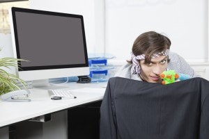 Portrait of young businessman aiming with toy gun at desk